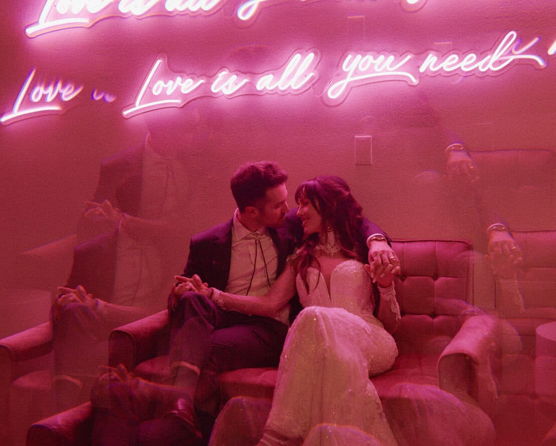 wedding couple sitting in front of pink neon signage